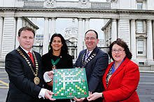 Four people holding a Scrabble game board in front of a large building