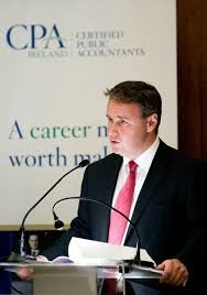 Man in a suit speaking at a Certified Public Accountants event podium with a backdrop reading "A career worth making."
