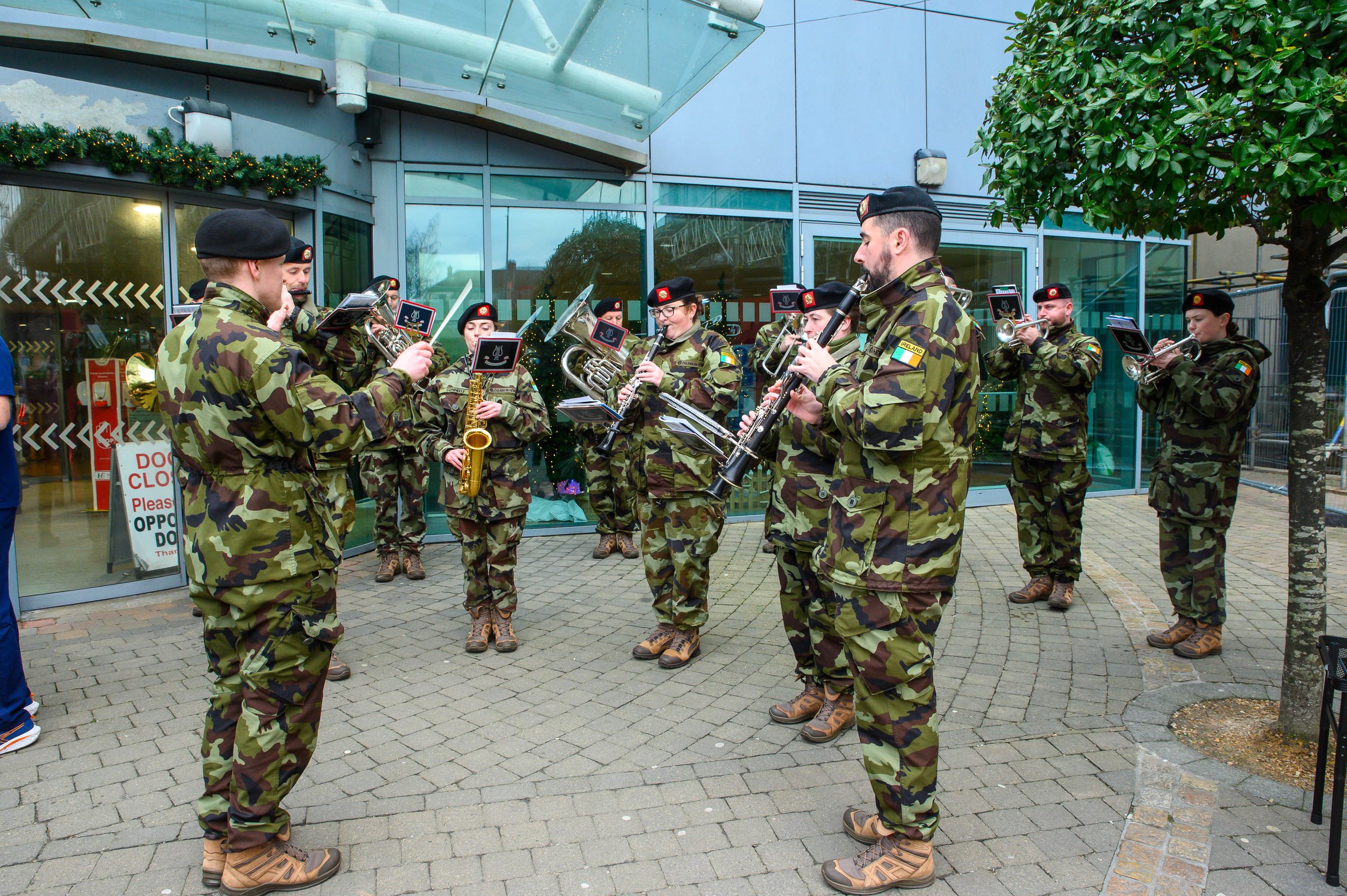 Army band in camouflage uniforms playing brass instruments outside a glass-fronted building at Christmas